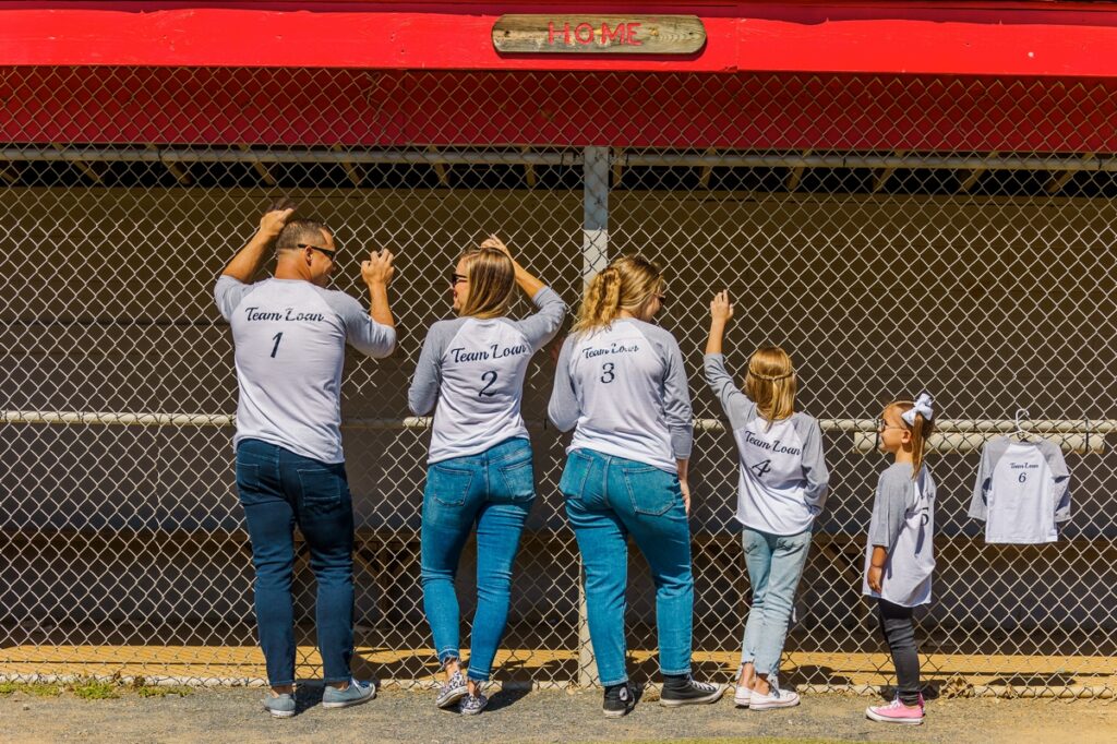 The Loan family showing off their matching t-shirts at a ball field captured by a maternity photographer in Virginia